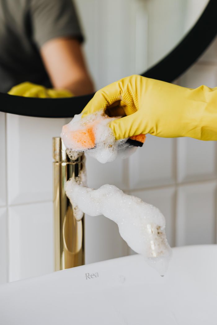 gallery-4 Anonymous person washing golden shiny faucet and sink in bathroom while wearing yellow latex glove during household care routine work