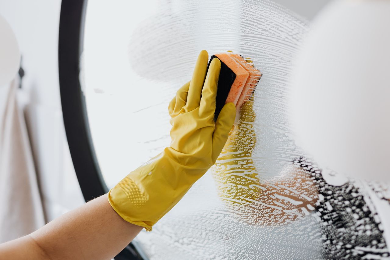 services-02 Anonymous person in yellow rubber gloves using simple sponge for cleaning mirror in bathroom