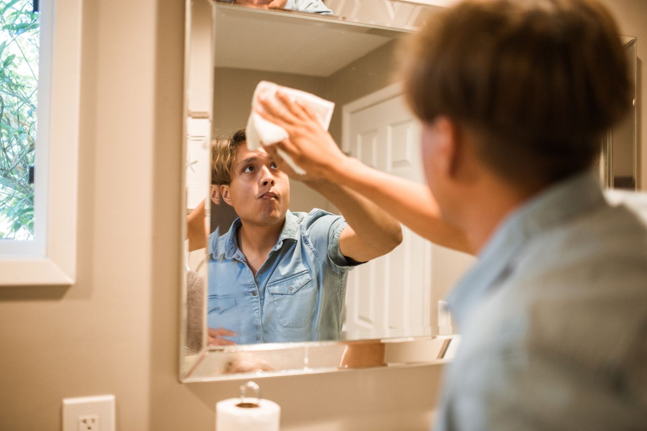 gallery-2 A man wiping a bathroom mirror, focusing on cleanliness and hygiene in a domestic setting.