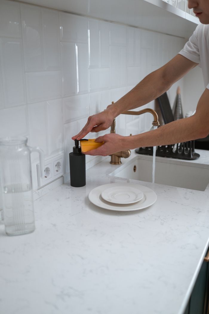 why-choose-us Close-up of hands washing dishes at a modern kitchen sink with white counter.
