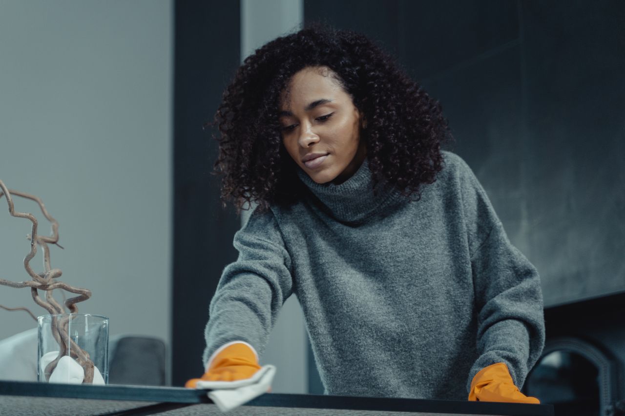 about-01 A woman in a gray sweater wipes a table with care, showcasing home cleaning in comfort.