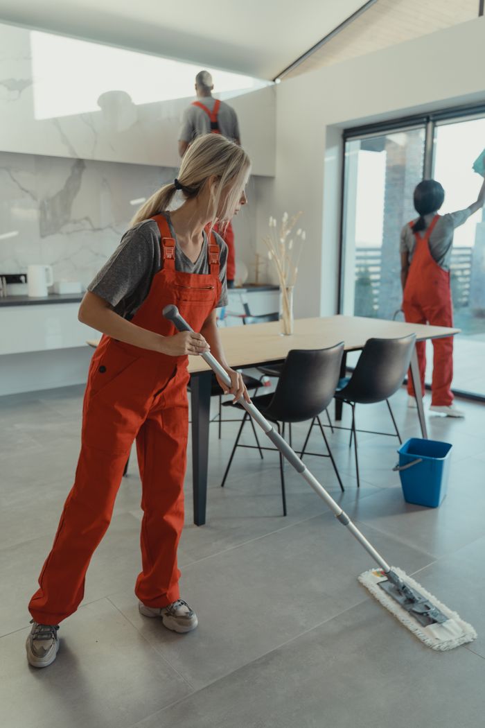gallery-6 Cleaning team in red overalls mopping and sanitizing a modern home interior.