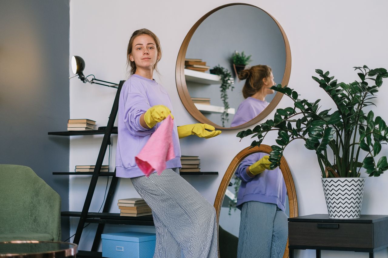gallery-5 Side view of cheerful woman in casual clothes and latex gloves standing near mirrors while cleaning apartment in daytime